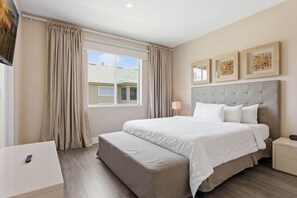 A bedroom with a large bed, a bedside table, a bench, a window with curtains, and wall-mounted artwork. - Upscale 3BR suites, Patio with BBQ & Jacuzzi (Four Corners)