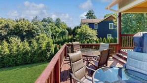Une terrasse dotée de mobilier d’extérieur, d’une table en verre et offrant une vue sur une maison et des arbres.