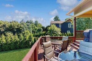 Eine Terrasse mit Gartenmöbeln, einem Glastisch und Blick auf ein Haus und Bäume.