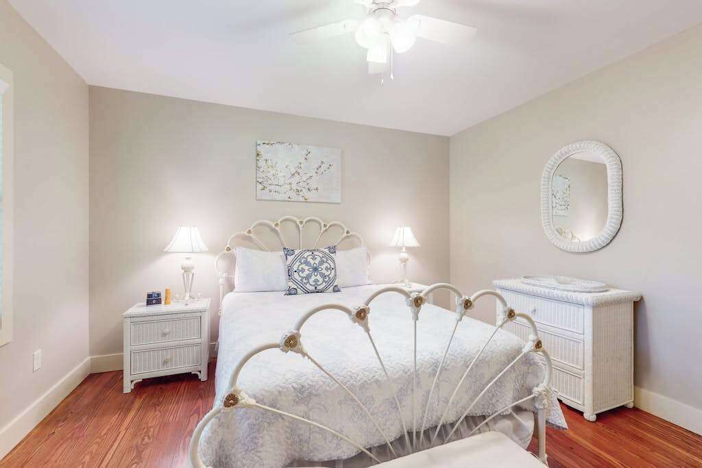 A bedroom with a bed, bedside tables, a dresser, a ceiling fan, and a wall-mounted mirror.