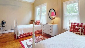 Un dormitorio con dos camas, ventilador de techo, cómoda, espejo y ventana con cortinas.