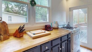 Una cocina con encimera de madera, estufa a gas y un amplio ventanal con vistas a árboles.