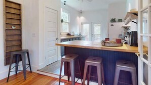 Una cocina con una isla de madera, taburetes de bar, un ventilador de techo y vistas al área de comedor contigua.