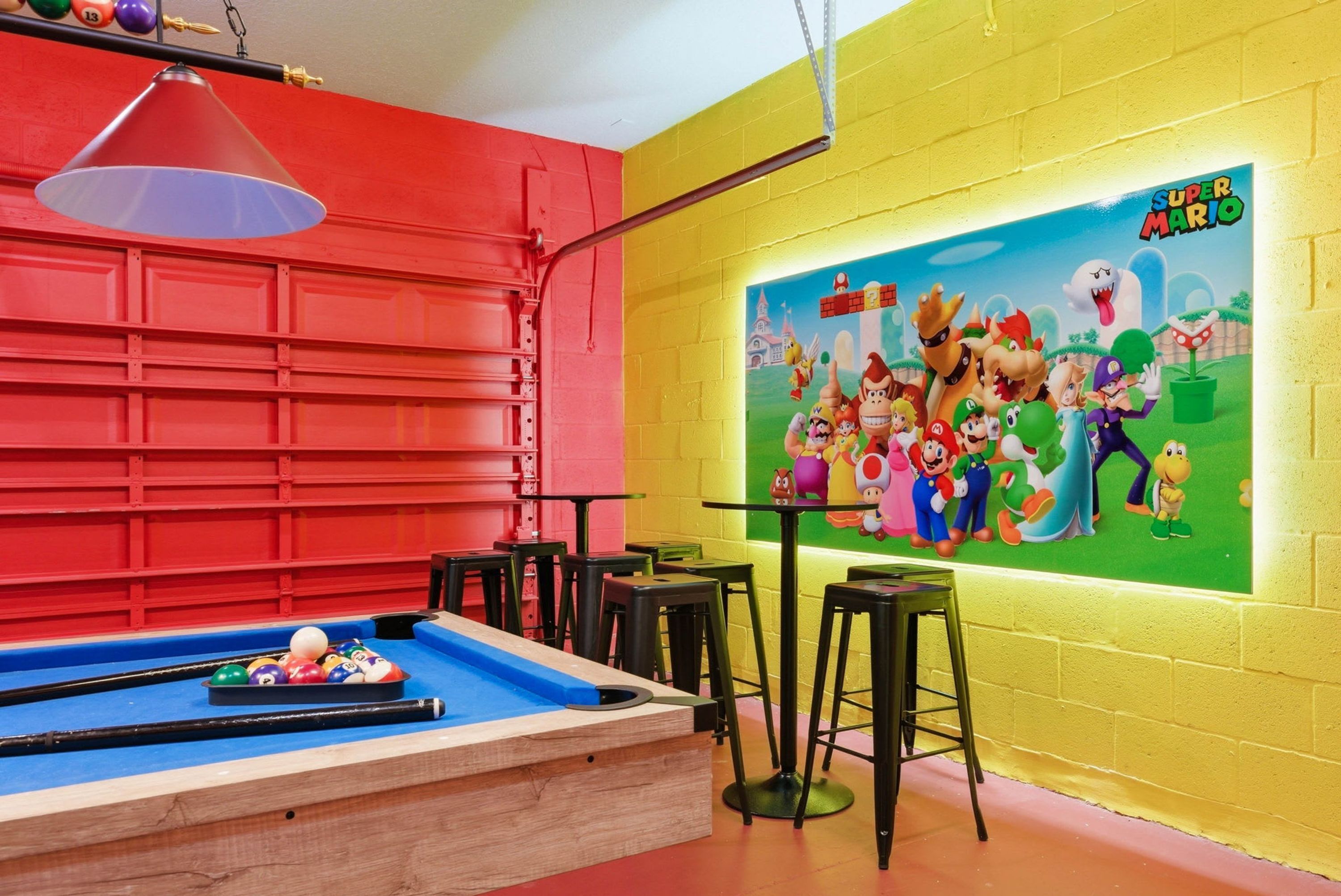 A colorful room with a pool table, a mural of Super Mario characters, and a red wall.