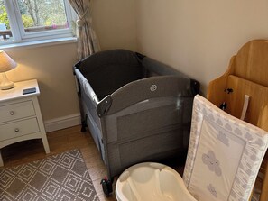 Ein Zimmer mit einer grauen Wickelstation, einer weißen Toilette, einem Holzschrank, einem weißen Nachttisch mit einer Lampe und einem gemusterten Teppich.