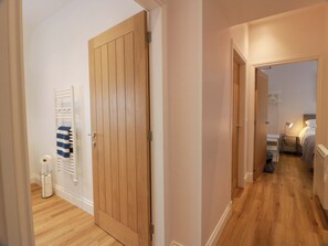 A hallway with a wooden door, a radiator, and a bed with a lamp. - Burnside Bothy (Girvan)
