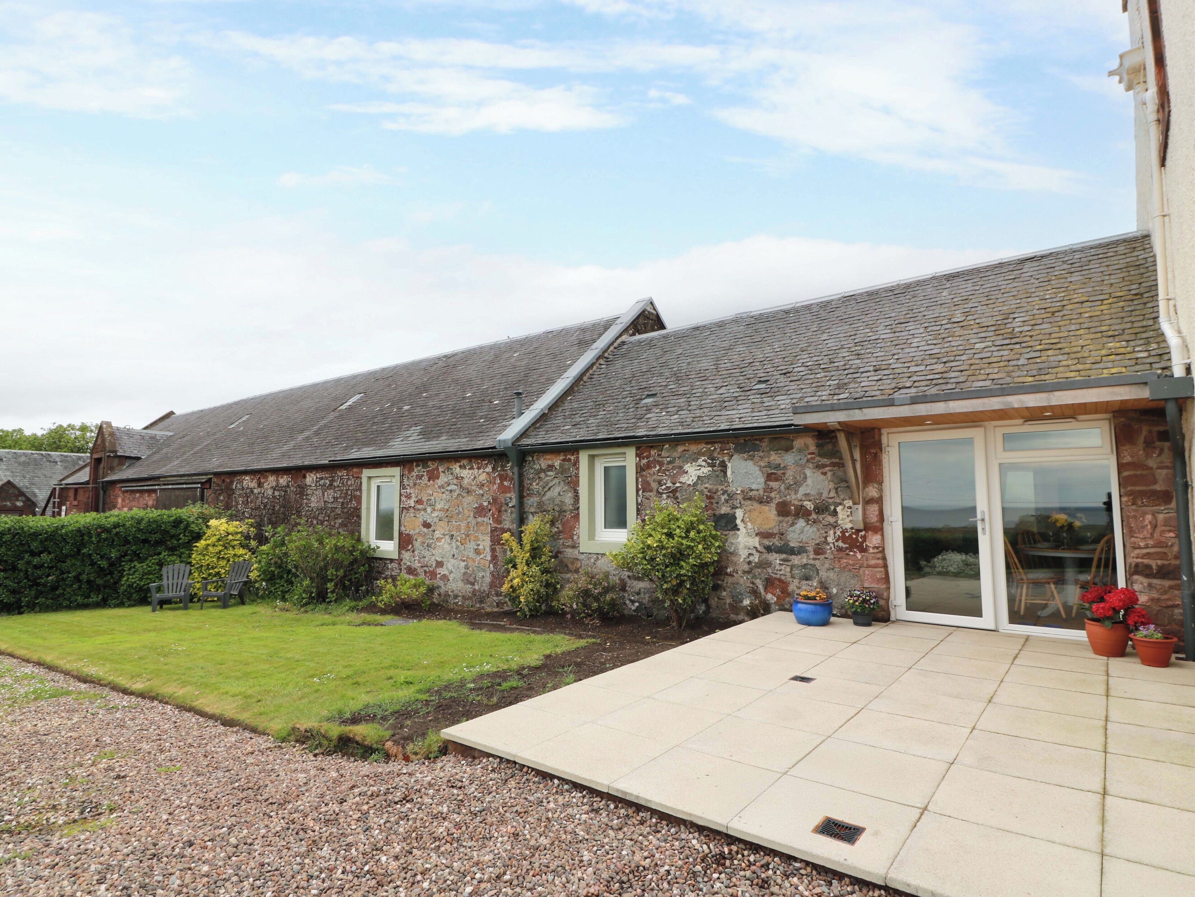 A stone building with a tiled patio, a grassy lawn, and a hedge.