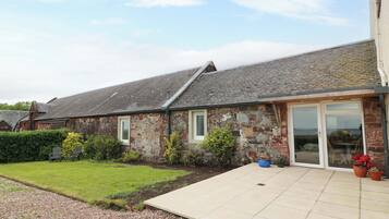 A stone building with a tiled patio, a grassy lawn, and a hedge.