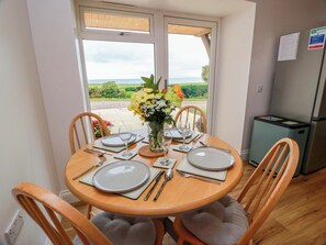 Un comedor con una mesa preparada para cuatro personas, un florero con flores y vistas al exterior.