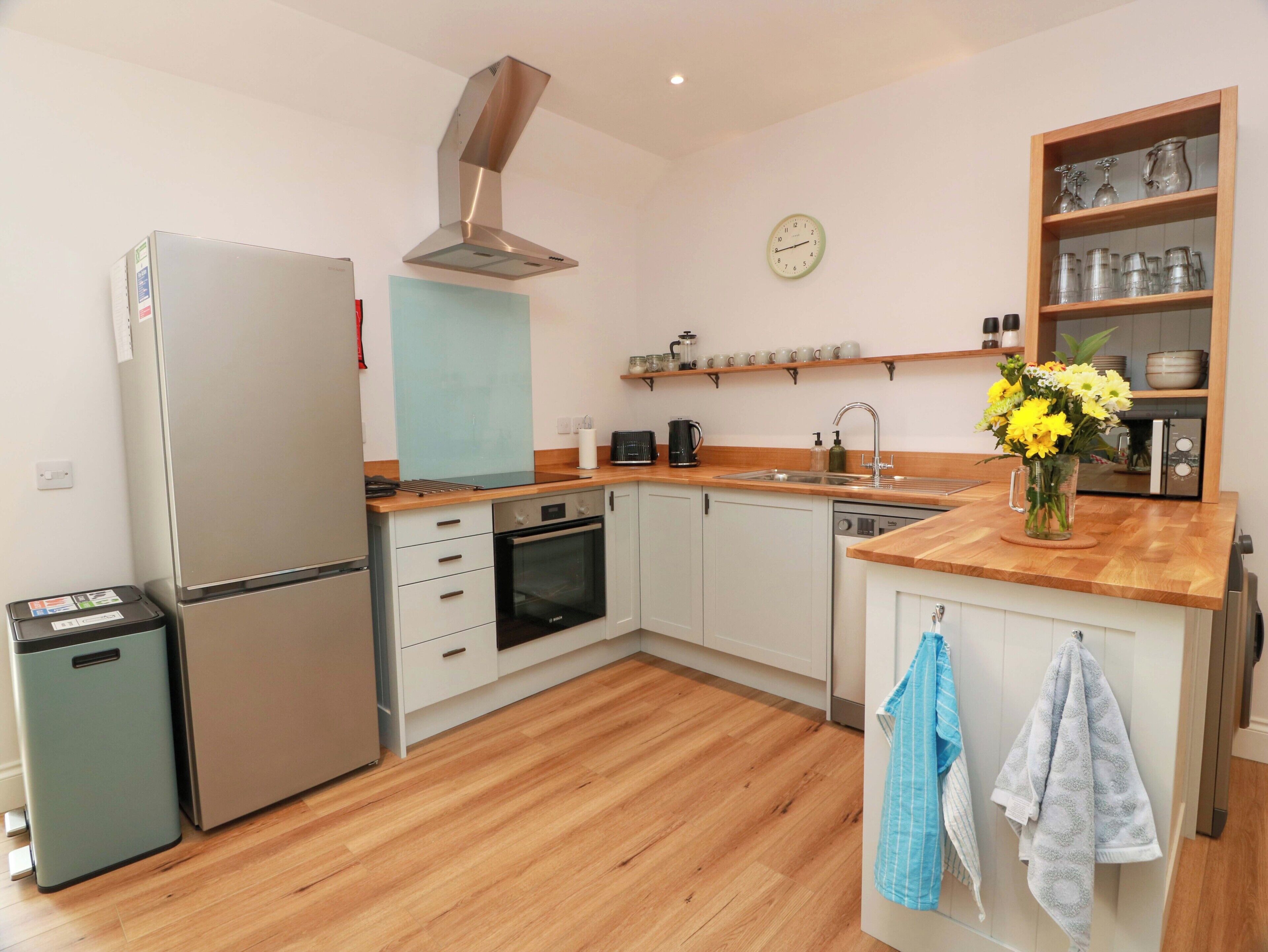 A modern kitchen with a stainless steel refrigerator, oven, and dishwasher, wooden countertops, and a clock on the wall.