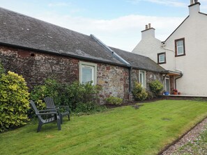 A stone house with a sloped roof, a front door, and a small porch with potted plants. - Burnside Bothy (Girvan)