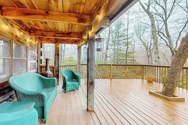 Eine Holzterrasse mit Korbmöbeln, einer Laterne und Blick auf Bäume.