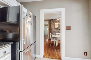 A kitchen with a stainless steel refrigerator, a dining area with a stone wall, and a wooden floor. - Vintage home with modern updates - near Biltmore, Chimney Rock & Lake Lure (Fletcher)
