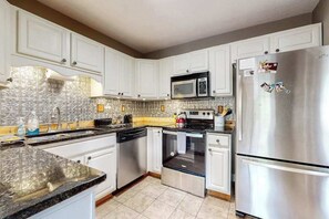 A kitchen with white cabinets, a stainless steel refrigerator, a microwave, and a dishwasher. - Vintage home with modern updates - near Biltmore, Chimney Rock & Lake Lure (Fletcher)
