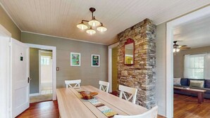Uma área de refeições com mesa de madeira, cadeiras brancas, parede decorada com pedra e um ventilador de teto.