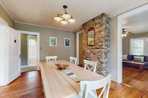 A dining area with a wooden table, white chairs, a stone accent wall, and a ceiling fan. - Vintage home with modern updates - near Biltmore, Chimney Rock & Lake Lure (Fletcher)