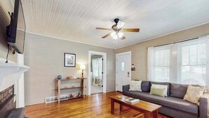 Uma sala de estar com piso de madeira, um sofá, uma mesa de centro, um ventilador de teto e uma lareira.