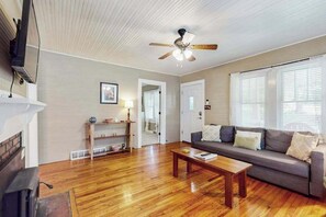 A living room with a wooden floor, a sofa, a coffee table, a ceiling fan, and a fireplace. - Vintage home with modern updates - near Biltmore, Chimney Rock & Lake Lure (Fletcher)