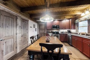 Une table à manger en bois, avec des chaises, un lustre et des meubles de rangement en bois dans une cuisine.