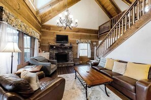 L’intérieur d’une cabane en rondins, avec une cheminée, des canapés en cuir, un lustre et un escalier.