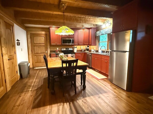 Una cocina con armarios de madera, un refrigerador de acero inoxidable, una mesa de comedor con sillas y una lámpara colgante.