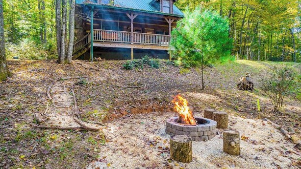 Une cabane dotée d’une véranda, d’un foyer extérieur et entourée d’une forêt.