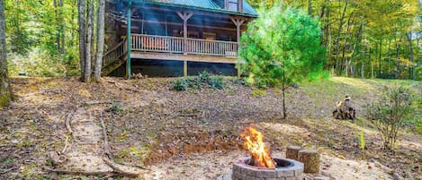 A cabin with a porch, a fire pit, and a forested backdrop.
