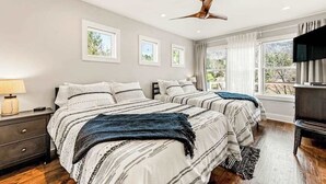 Une chambre avec deux lits, un ventilateur de plafond, une télévision et une fenêtre avec des rideaux.