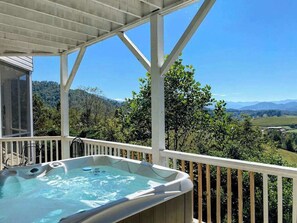 Ein Whirlpool auf einer Holzterrasse mit Blick auf einen Wald und Berge.