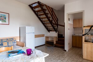 A compact kitchen with a wooden staircase, a dining area with a table and chairs, and a refrigerator. - Nice House With Garden and Pool in Bibione (San Michele al Tagliamento)