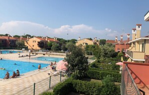 A swimming pool area with multiple pools, surrounded by residential buildings with red-tiled roofs. - Nice House With Garden and Pool in Bibione (San Michele al Tagliamento)