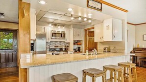 A kitchen with a central island, wooden stools, white cabinets, and a 'HOME' sign above the island. - Angel View (Cullowhee)