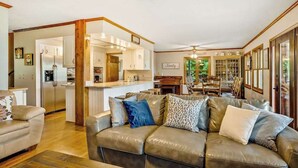 A spacious living area with a leather sofa, wooden beams, a kitchen in the background, and a dining area with chairs. - Angel View (Cullowhee)