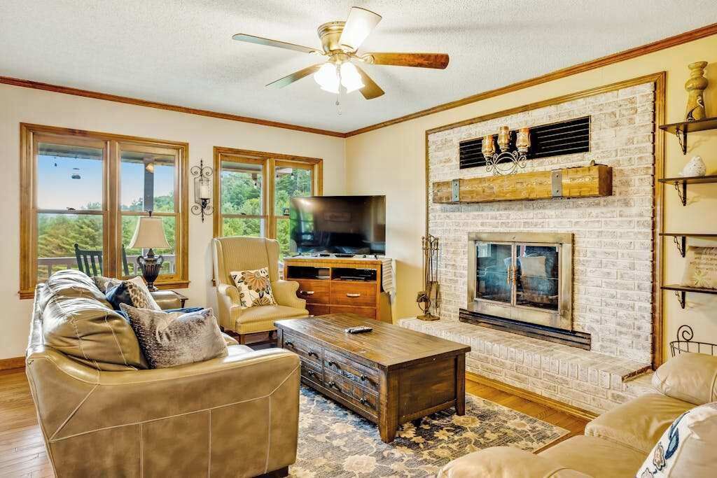 A living room with a fireplace, leather sofas, a TV, and a ceiling fan.