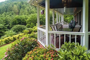 Eine überdachte Veranda mit Gartenmöbeln, umgeben von üppiger Vegetation und Blick auf einen bewaldeten Hang.