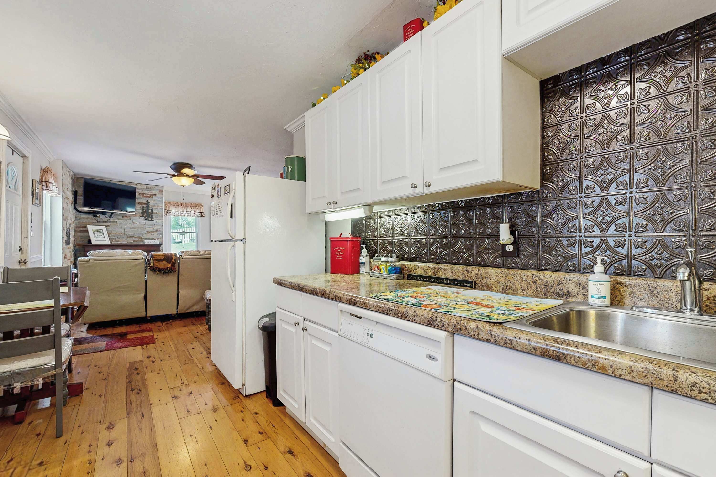 A kitchen with white cabinets, a granite countertop, a dishwasher, and a decorative backsplash.