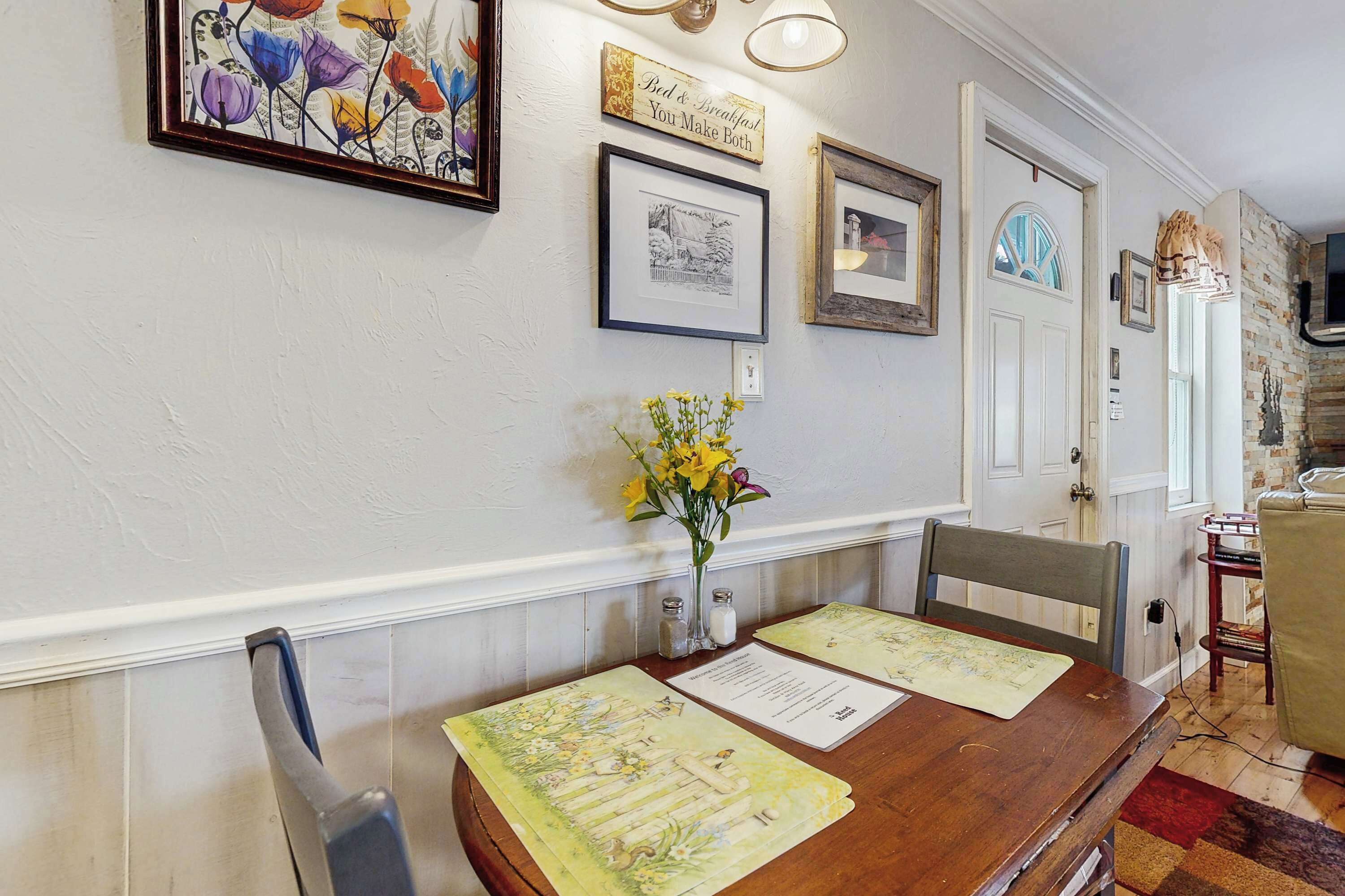 A dining area with a wooden table, framed artwork, and a vase with flowers.