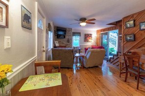 A cozy living room with a fireplace, a dining area with a table and chairs, and a kitchen area with a television. - Downtown, dog-friendly, Dillsboro home w/ fireplace - front porch & back deck (Dillsboro)
