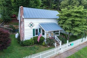 A white house with a metal roof, a porch, and a white picket fence. - Downtown, dog-friendly, Dillsboro home w/ fireplace - front porch & back deck (Dillsboro)