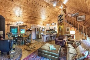 Ein gemütliches Blockhaus-Interieur mit Holzbalkendecke, Essbereich, Küche und Wohnzimmer mit Kamin.