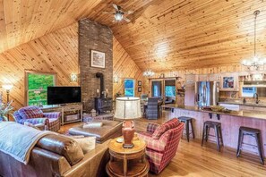 Ein gemütliches Blockhaus mit Wohnzimmer, Küche und Essbereich, mit Holzwänden und -decke, Kamin und Fernseher.