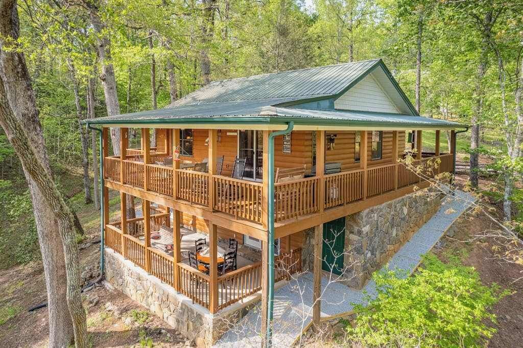 A two-story log cabin with a balcony, surrounded by trees.