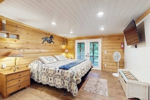 Ein Schlafzimmer mit Holzwänden, einem Bett, Nachttischlampen, einem Fernseher und einem Ventilator.
