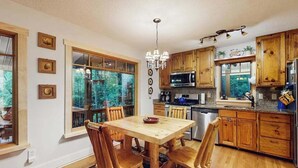 Una cocina con armarios de madera, una mesa de comedor con sillas, una araña y vistas a través de las ventanas.
