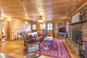 Ein Holzblockhaus-Interieur mit Kamin, einer Couch, einem Couchtisch und einem Essbereich.