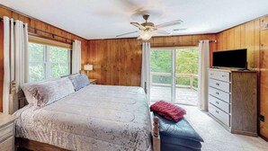 Een slaapkamer met een bed, een plafondventilator, een televisie, een dressoir en een raam.