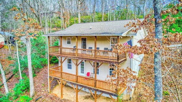 A two-story wooden cabin with a balcony, surrounded by trees.