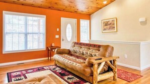 A room with a wooden ceiling, a sofa, a rug, and a painting on the wall.