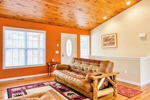 A room with a wooden ceiling, a sofa, a rug, and a painting on the wall. - Trimont Mountain Cottage (Franklin)