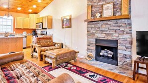 A cozy living room with a stone fireplace, wooden furniture, and a kitchen area with wooden cabinets and a microwave.